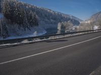 a large car driving on the highway in front of a snowy forest covered hillsides