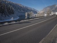 a large car driving on the highway in front of a snowy forest covered hillsides