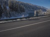 a large car driving on the highway in front of a snowy forest covered hillsides