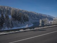 a large car driving on the highway in front of a snowy forest covered hillsides