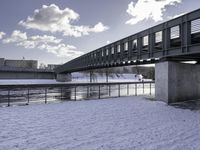 the snow on the ground is covering the ground below a bridge with clouds and water