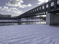 the snow on the ground is covering the ground below a bridge with clouds and water