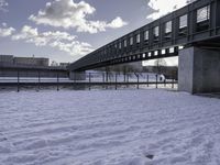 the snow on the ground is covering the ground below a bridge with clouds and water