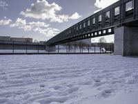 the snow on the ground is covering the ground below a bridge with clouds and water