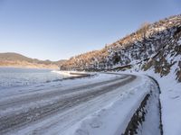 a narrow road lined with snow next to the ocean and a cliff covered in snow