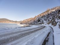 a narrow road lined with snow next to the ocean and a cliff covered in snow