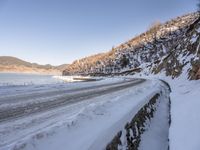 a narrow road lined with snow next to the ocean and a cliff covered in snow