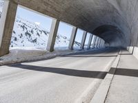 this is a long tunnel in the mountains where there is snow covering the ground and a person riding a skateboard