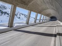 this is a long tunnel in the mountains where there is snow covering the ground and a person riding a skateboard