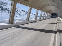 this is a long tunnel in the mountains where there is snow covering the ground and a person riding a skateboard