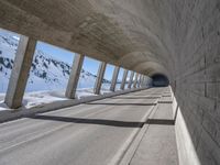 this is a long tunnel in the mountains where there is snow covering the ground and a person riding a skateboard