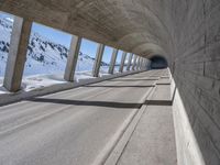 this is a long tunnel in the mountains where there is snow covering the ground and a person riding a skateboard