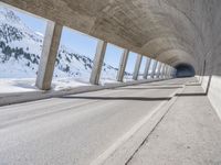 this is a long tunnel in the mountains where there is snow covering the ground and a person riding a skateboard