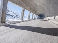 this is a long tunnel in the mountains where there is snow covering the ground and a person riding a skateboard