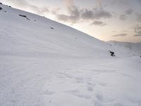 a man riding a snowboard down the side of a snow covered hill while skiing