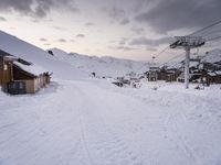 skiiers are skiing down a snow covered slope at sunset in a city with large mountains in the background