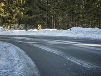 the road is lined with snow and trees in the background, there is a road sign