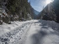 a long road that has been cleared by snow next to some woods and mountains with trees in the background