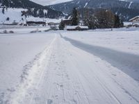 the snow and ski slope is covered in tracks and snow, with mountains and houses in the background