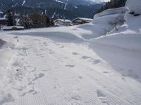 the snow and ski slope is covered in tracks and snow, with mountains and houses in the background
