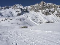 someone on skis stands in a deep snow field with mountains behind them and many footprints in the snow