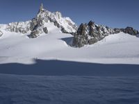 a lone person skis in the snow in front of a mountain peak with a shadow on it