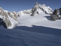 a lone person skis in the snow in front of a mountain peak with a shadow on it