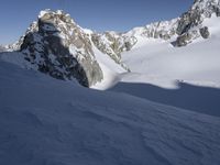 a lone person skis in the snow in front of a mountain peak with a shadow on it