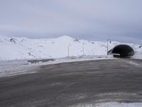 a car driving through a tunnel that goes out from snow - covered mountains below the highway