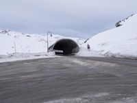 a car driving through a tunnel that goes out from snow - covered mountains below the highway