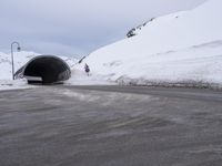 a car driving through a tunnel that goes out from snow - covered mountains below the highway