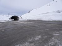 a car driving through a tunnel that goes out from snow - covered mountains below the highway