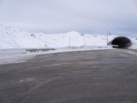 a car driving through a tunnel that goes out from snow - covered mountains below the highway