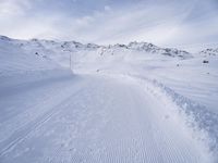 snow covered slope in the middle of a ski area as people ski on it near ski lift