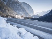 mountains are in the distance behind a snowy lake and road with snow on it and a building in the distance