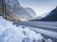 mountains are in the distance behind a snowy lake and road with snow on it and a building in the distance