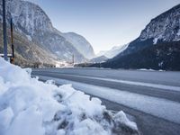 mountains are in the distance behind a snowy lake and road with snow on it and a building in the distance