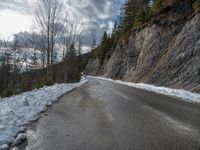 the road is lined by rocks and snow in the distance are trees, and mountains