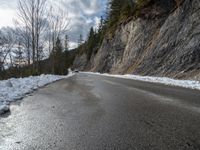 the road is lined by rocks and snow in the distance are trees, and mountains