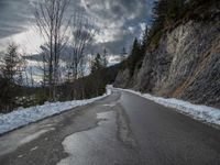 the road is lined by rocks and snow in the distance are trees, and mountains