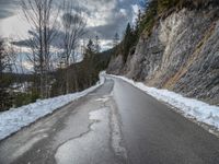 the road is lined by rocks and snow in the distance are trees, and mountains