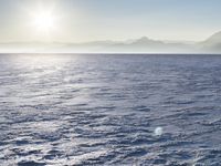 a snow - covered ocean with mountains in the distance and one boat floating near it