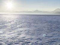 a snow - covered ocean with mountains in the distance and one boat floating near it