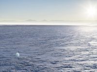 a snow - covered ocean with mountains in the distance and one boat floating near it