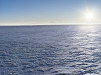 a snow - covered ocean with mountains in the distance and one boat floating near it