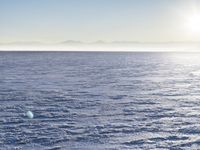 a snow - covered ocean with mountains in the distance and one boat floating near it