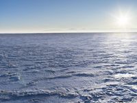 a snow - covered ocean with mountains in the distance and one boat floating near it