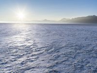 a snow - covered ocean with mountains in the distance and one boat floating near it