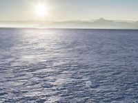 a snow - covered ocean with mountains in the distance and one boat floating near it