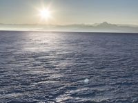 a snow - covered ocean with mountains in the distance and one boat floating near it
